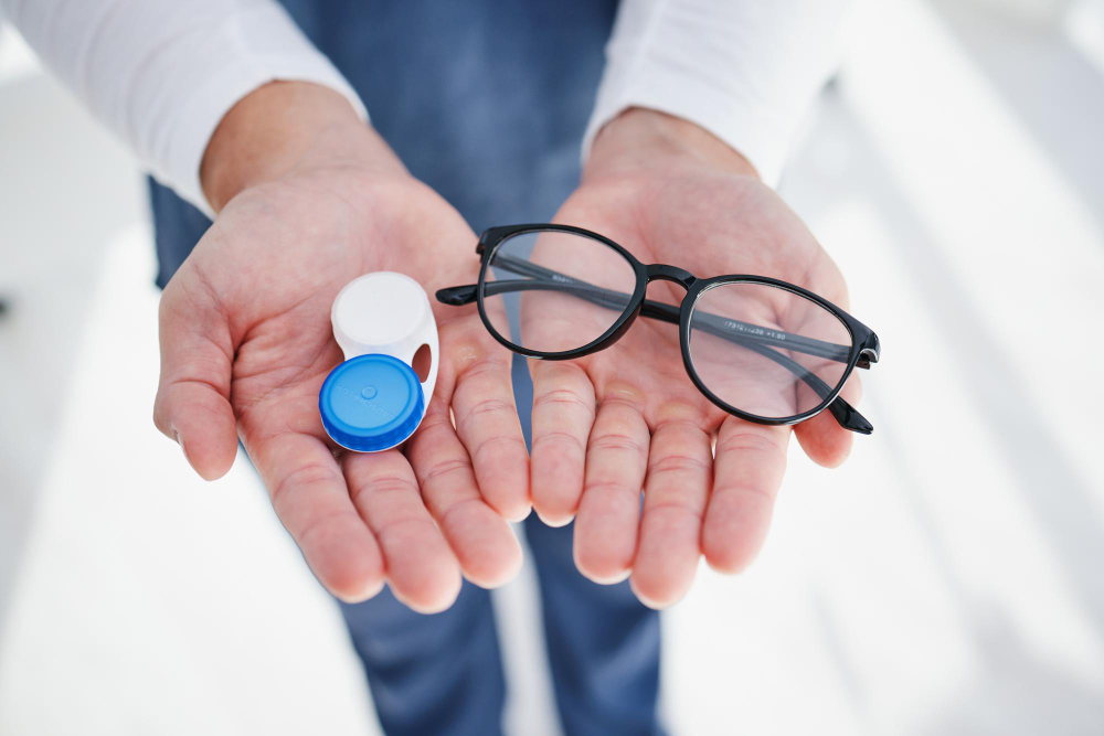 Deux mains d’un homme qui tends une paire de lunette ainsi qu’une pair de lentilles dans leur étui de protection blanc et bleu