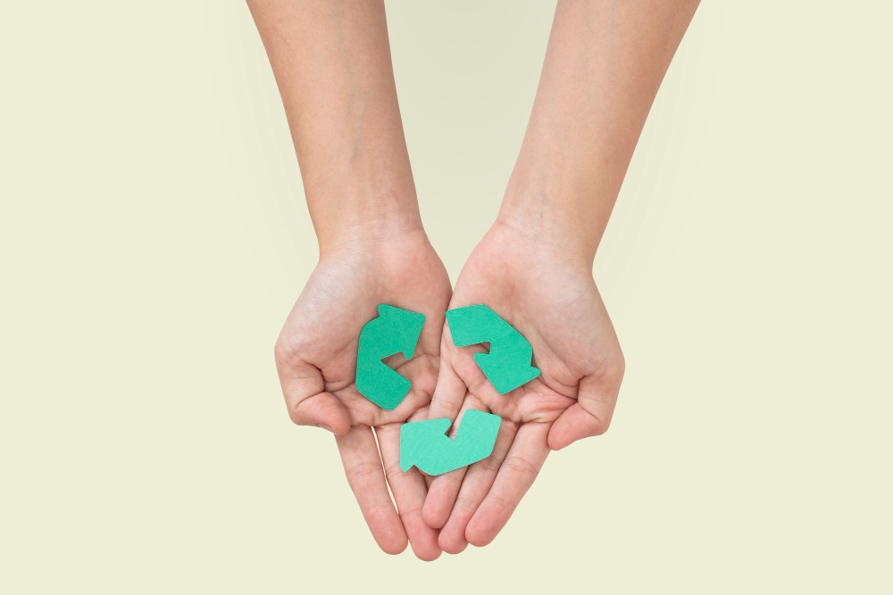 Une paire de main tiennnent et tendent vers l'avant un logo vert de recyclage