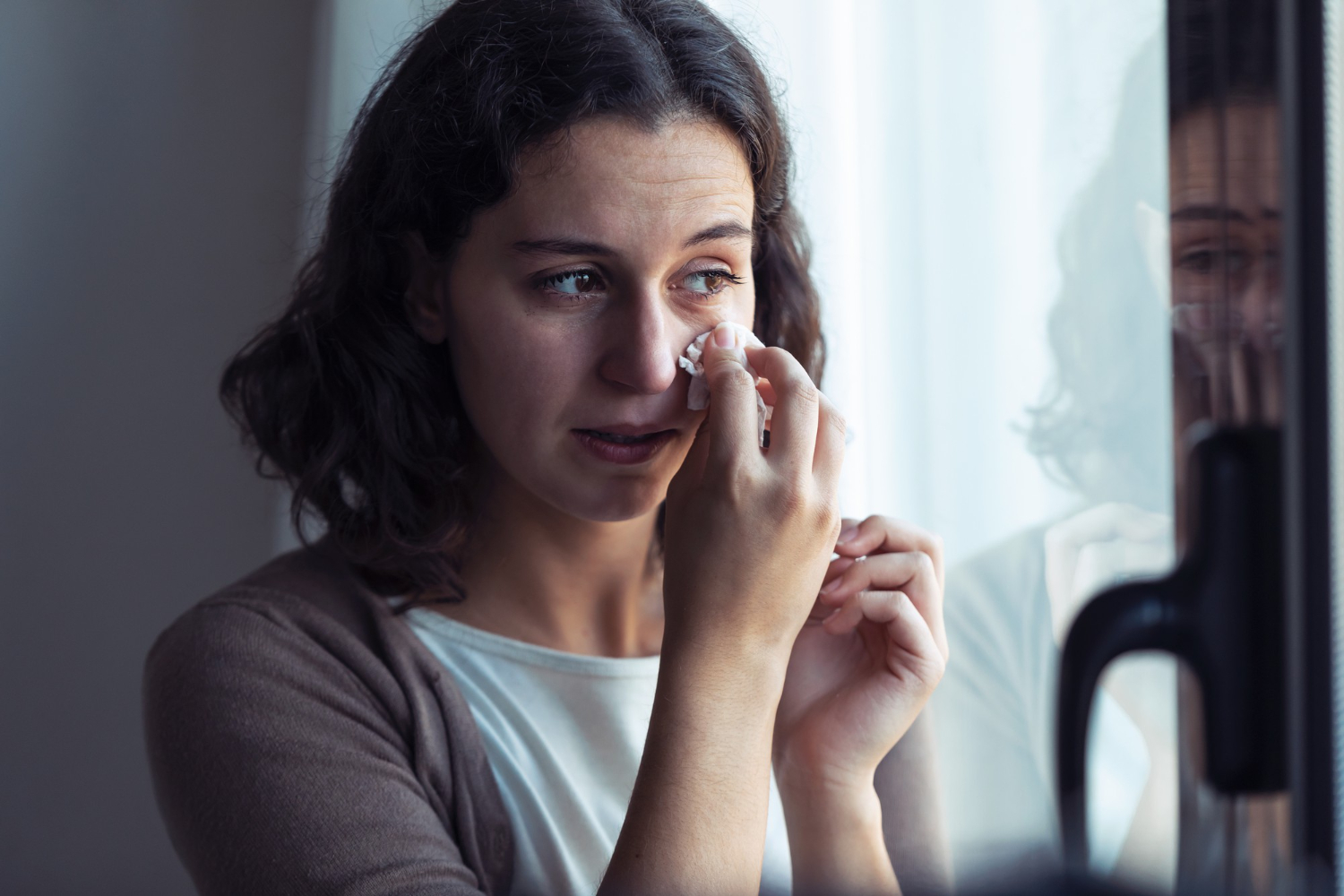Femme qui essuie ses larmes en regardant par la fenêtre