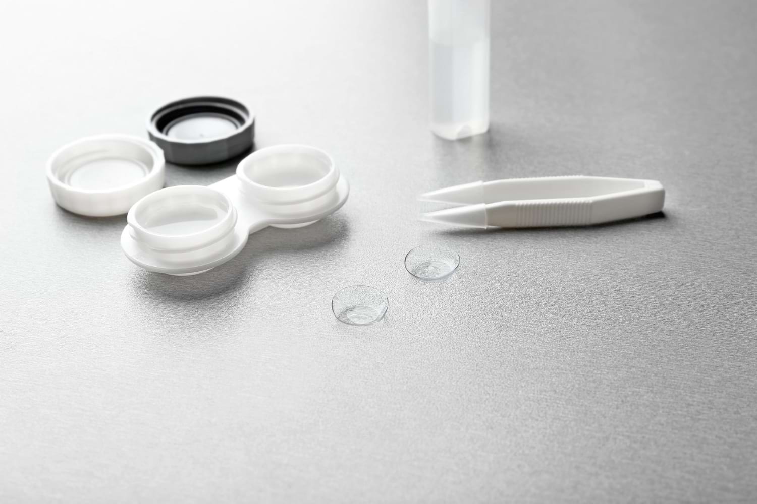 Paire de pincettes contenant des lentilles de contact et bouteille avec solution sur fond gris vue rapprochée